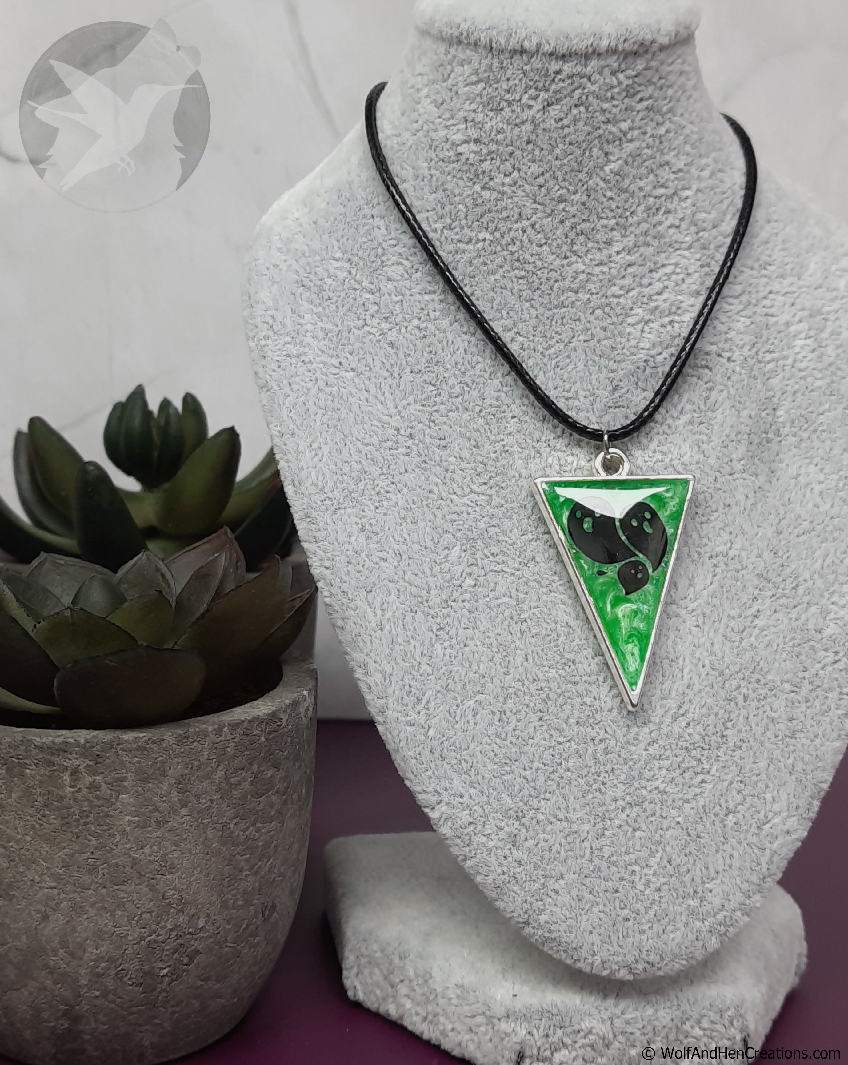 Necklace with a green triangular pendant featuring ghosts on a mannequin bust.