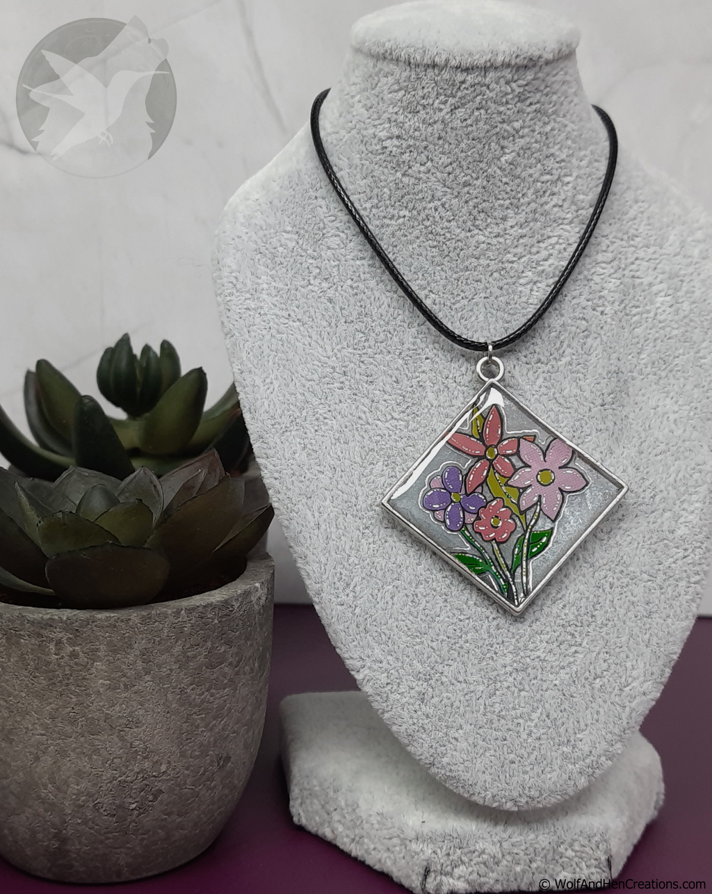 Necklace with a floral pendant on a mannequin bust next to a potted plant.