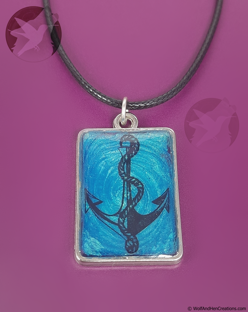 A rectangular pendant necklace featuring a black anchor illustration over a textured blue background, suspended from a black cord on a solid magenta background.