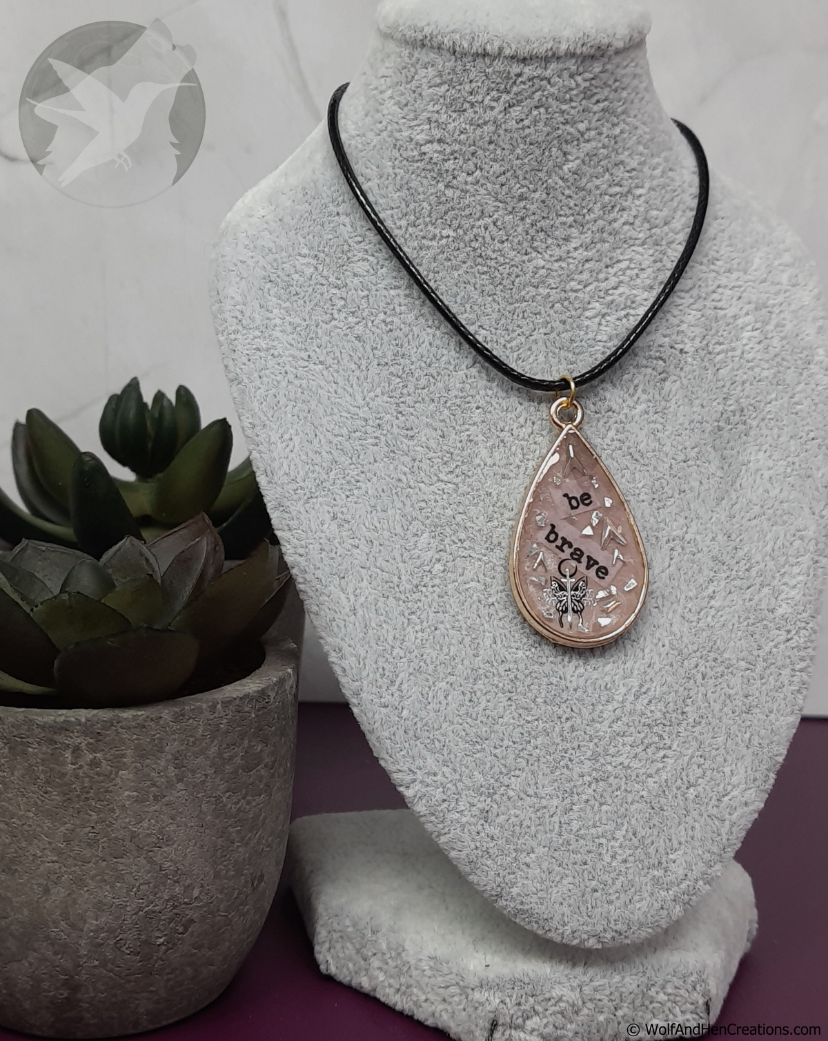 Necklace with a teardrop pendant on a mannequin bust, next to a potted plant.