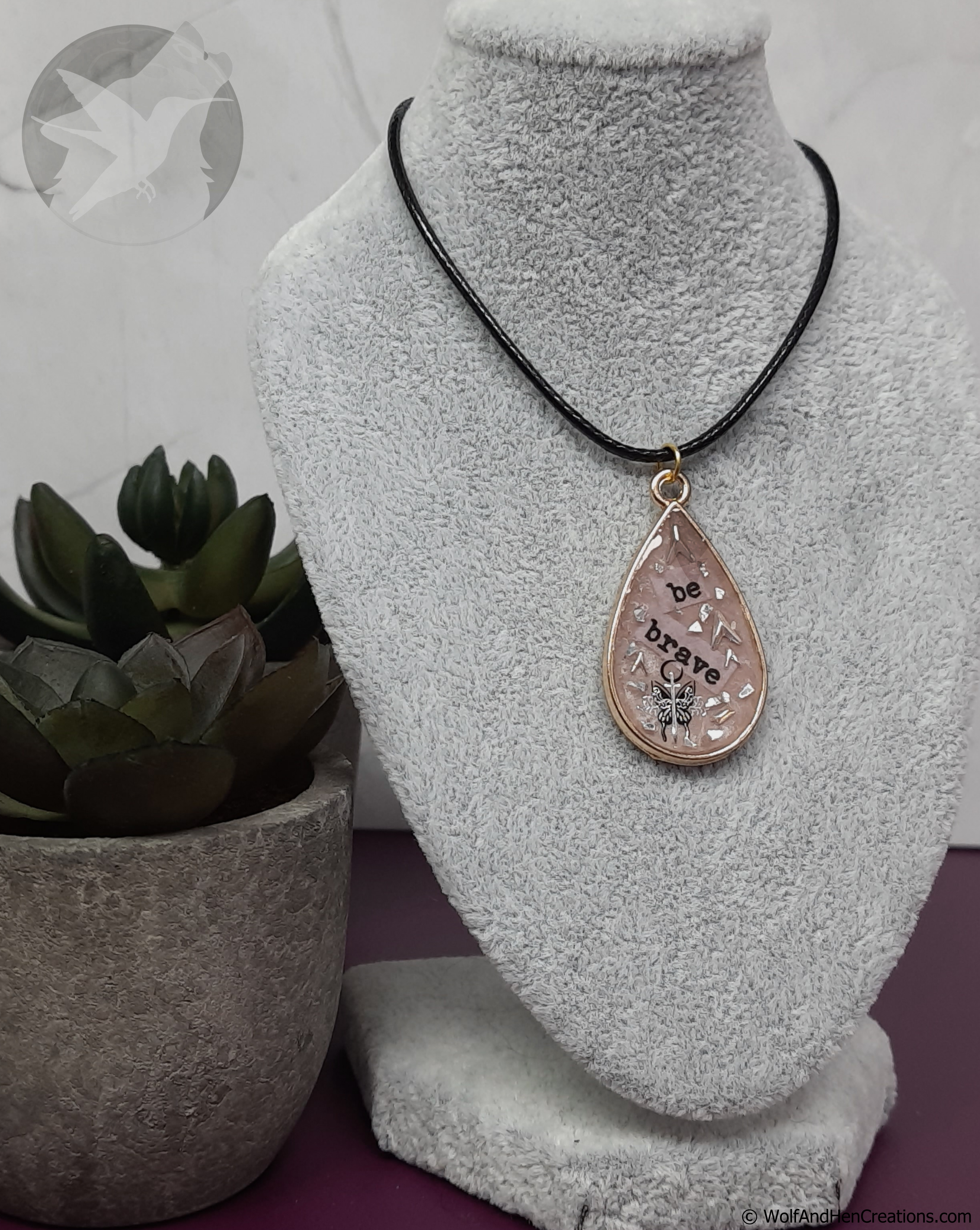 Necklace with a teardrop pendant on a mannequin bust, next to a potted plant.