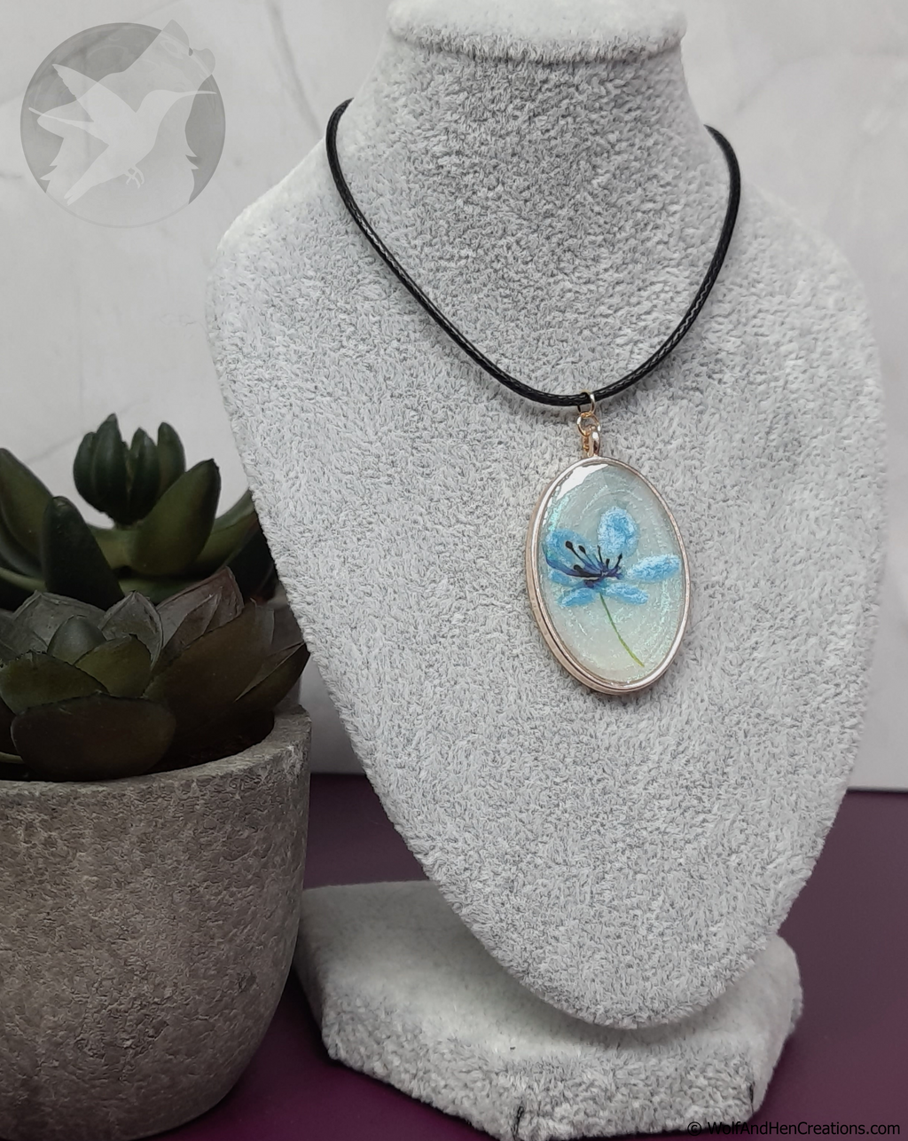 Necklace with a pendant on a mannequin bust next to a potted plant.