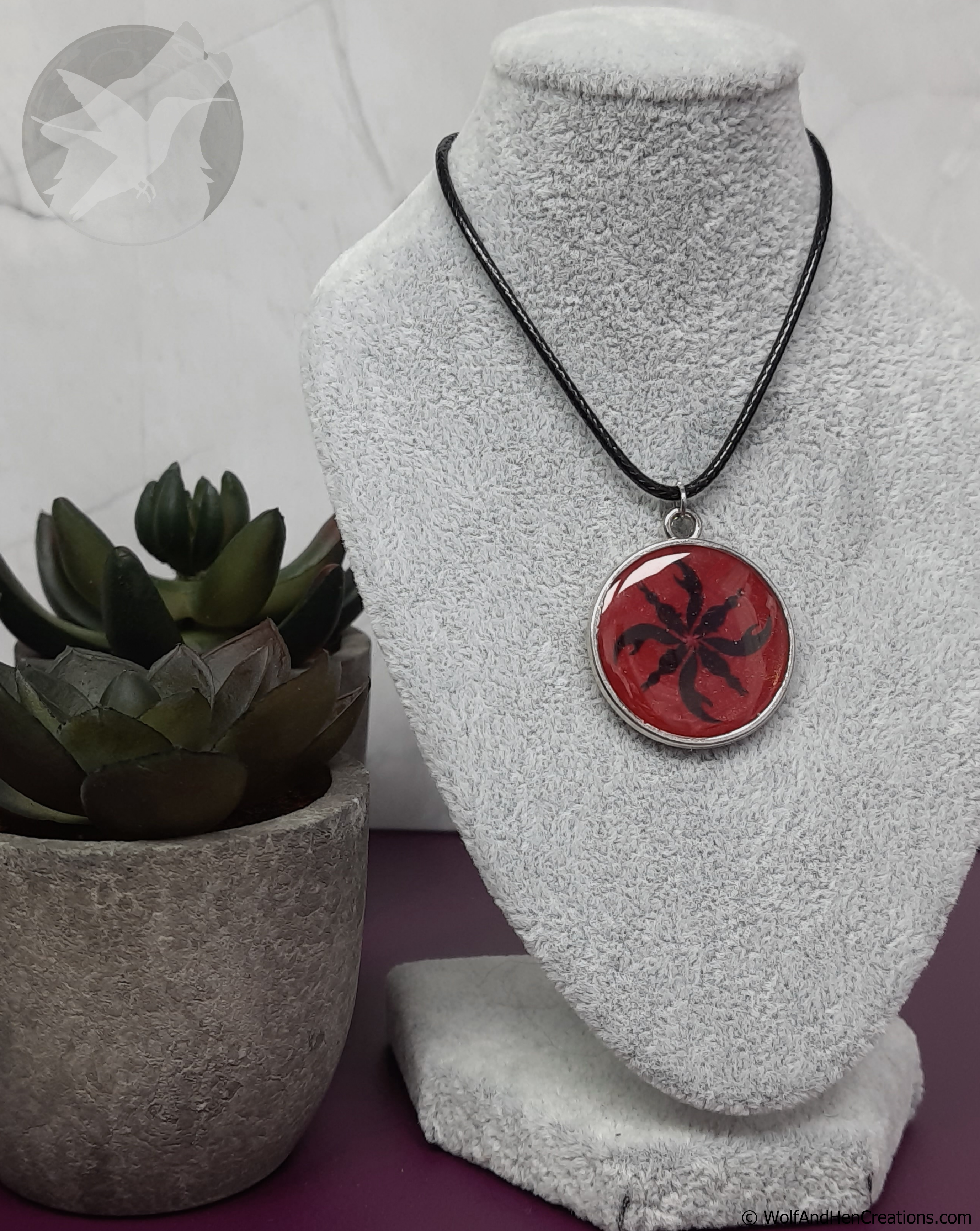 Necklace with a red pendant on a textured white stand, next to a potted plant.