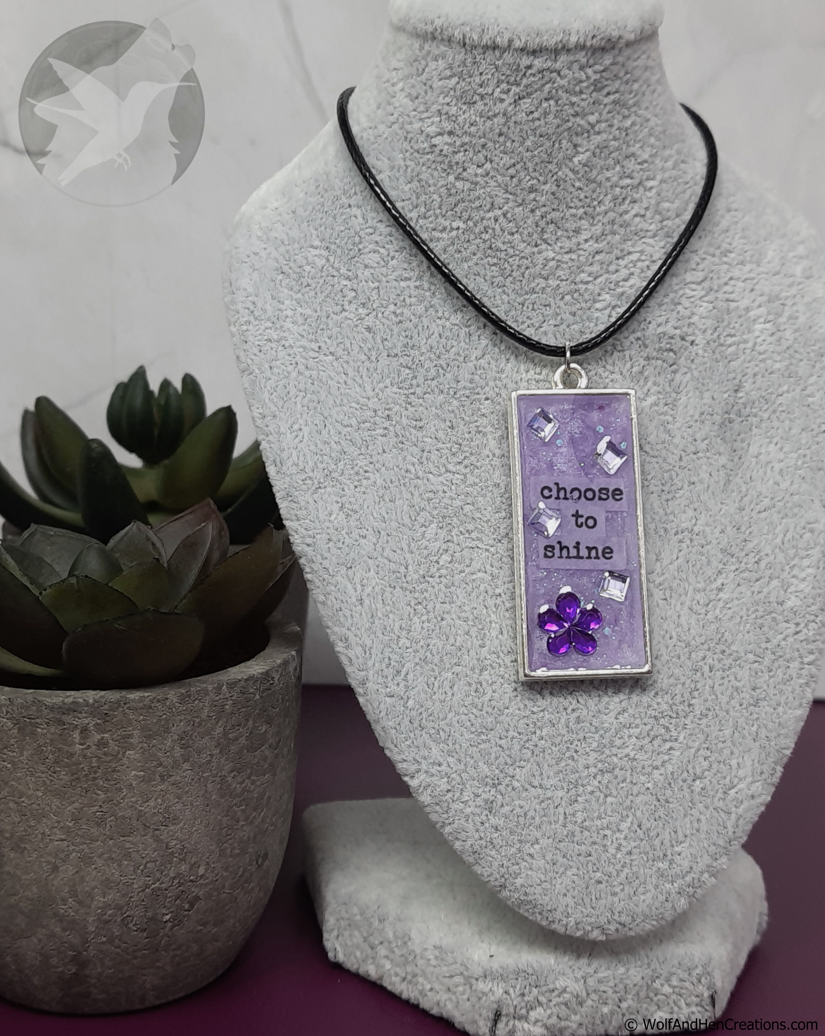 Necklace with a pendant on a gray bust, next to a potted plant.