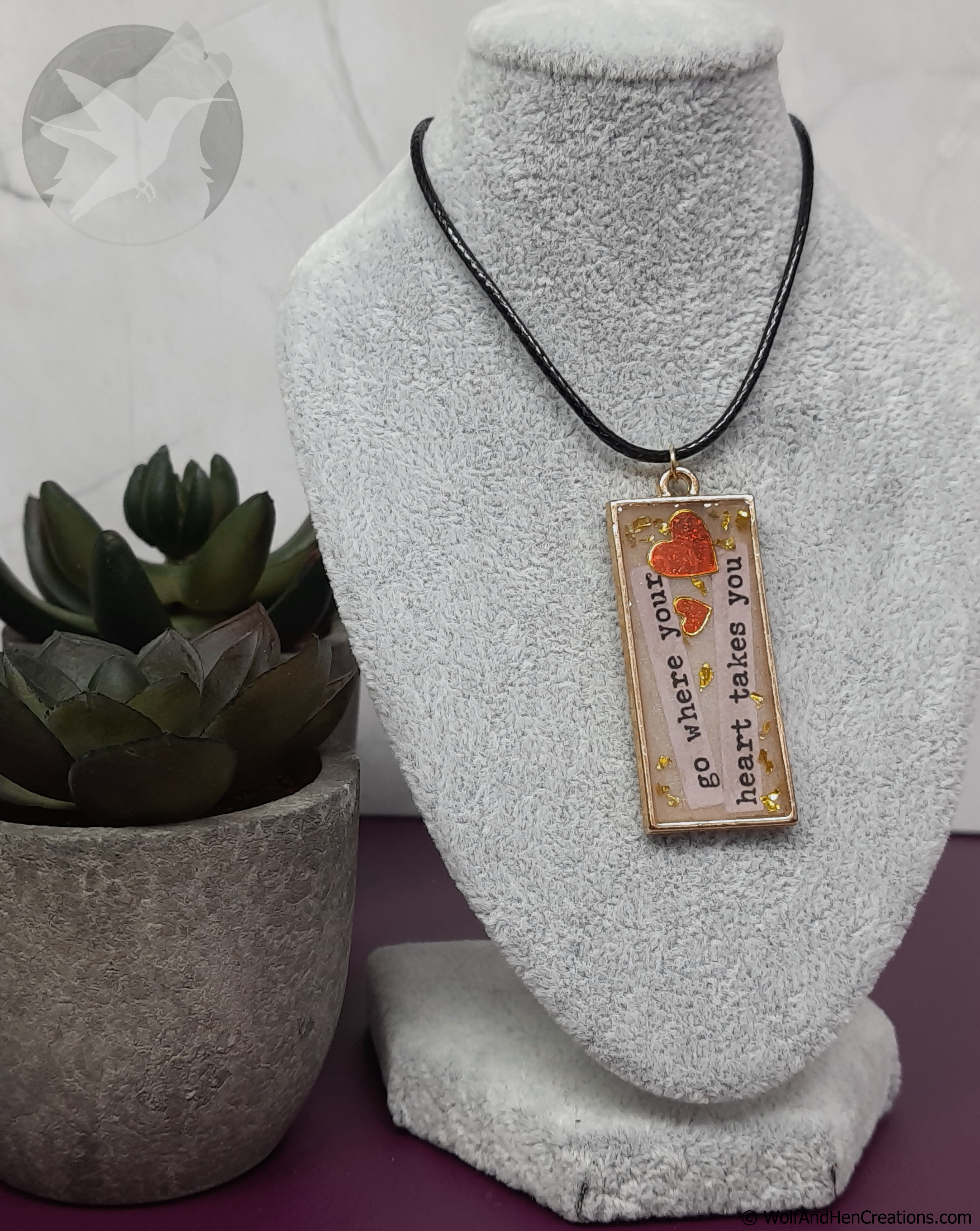 Necklace with a pendant on a white stand next to a potted plant
