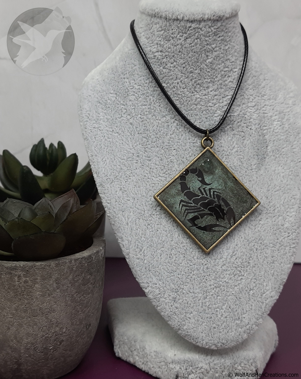 Necklace with a scorpion pendant on a gray bust, next to a potted plant.