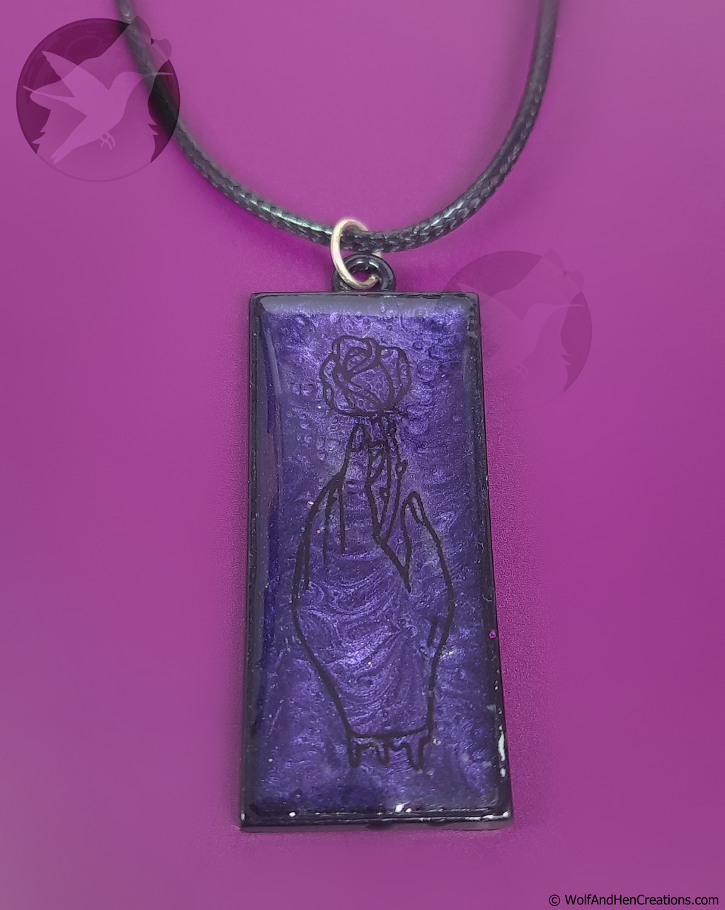 A rectangular purple pendant necklace featuring black line art of a bleeding hand grasping a rose, suspended from a black cord against a vibrant purple background.