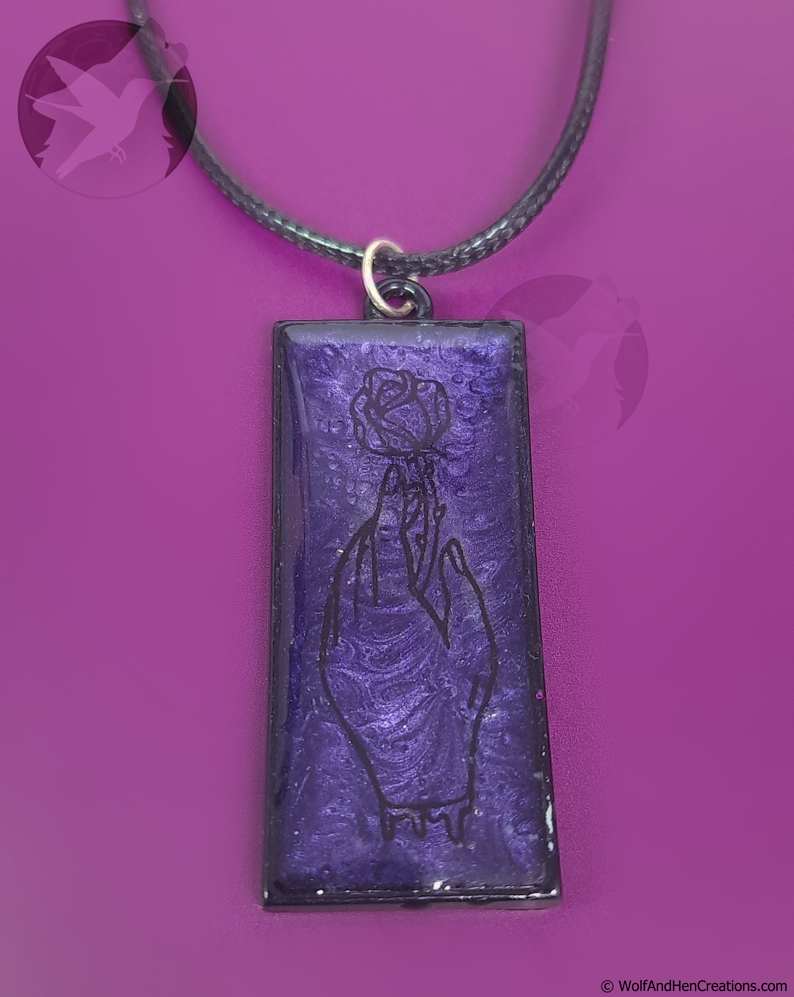 A rectangular purple pendant necklace featuring black line art of a bleeding hand grasping a rose, suspended from a black cord against a vibrant purple background.