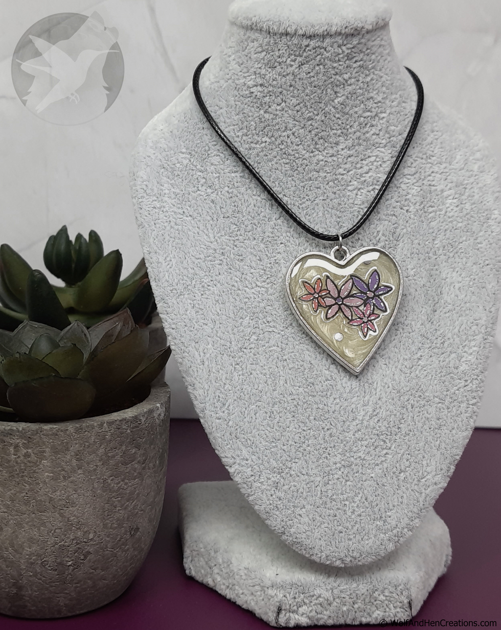 Heart-shaped pendant on a necklace displayed on a gray bust with a plant in the background