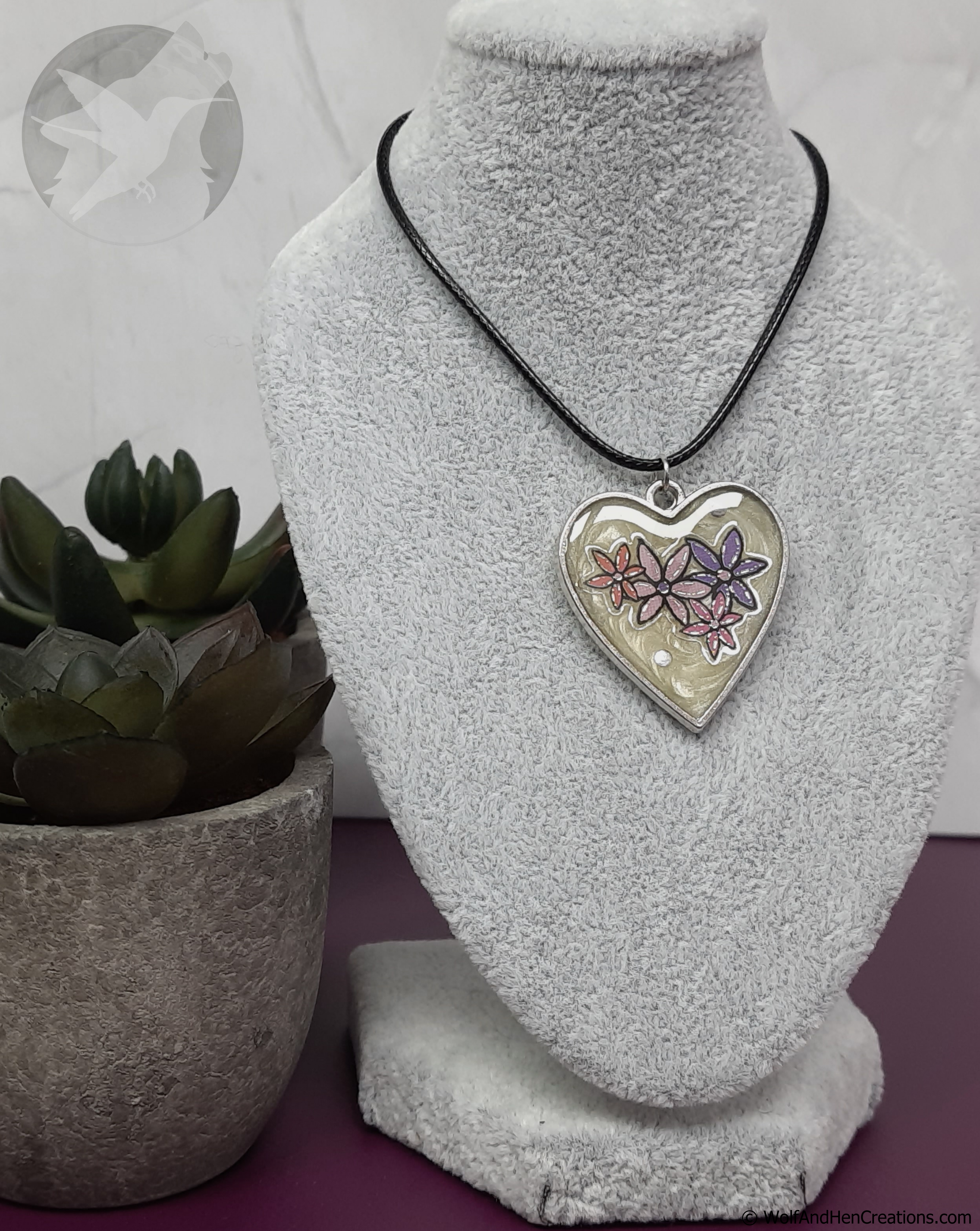 Heart-shaped pendant on a necklace displayed on a gray bust with a plant in the background