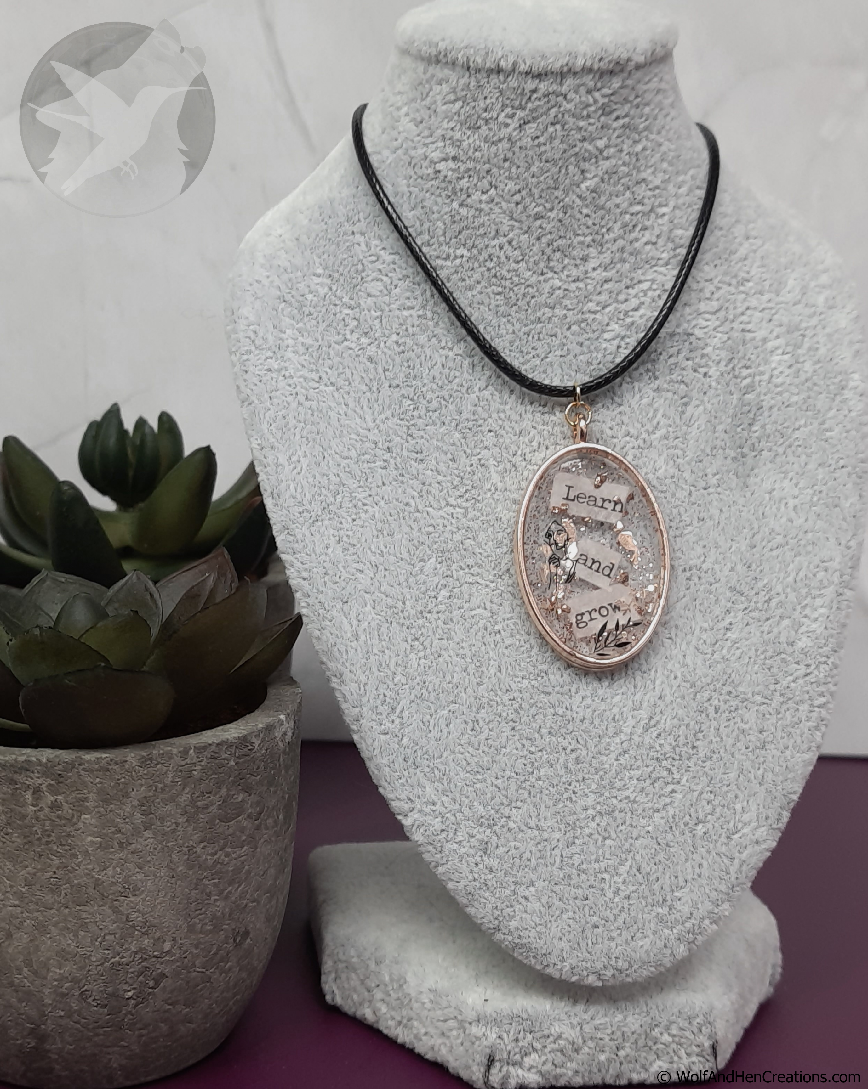 Necklace with a pendant on a gray bust, next to a potted plant.