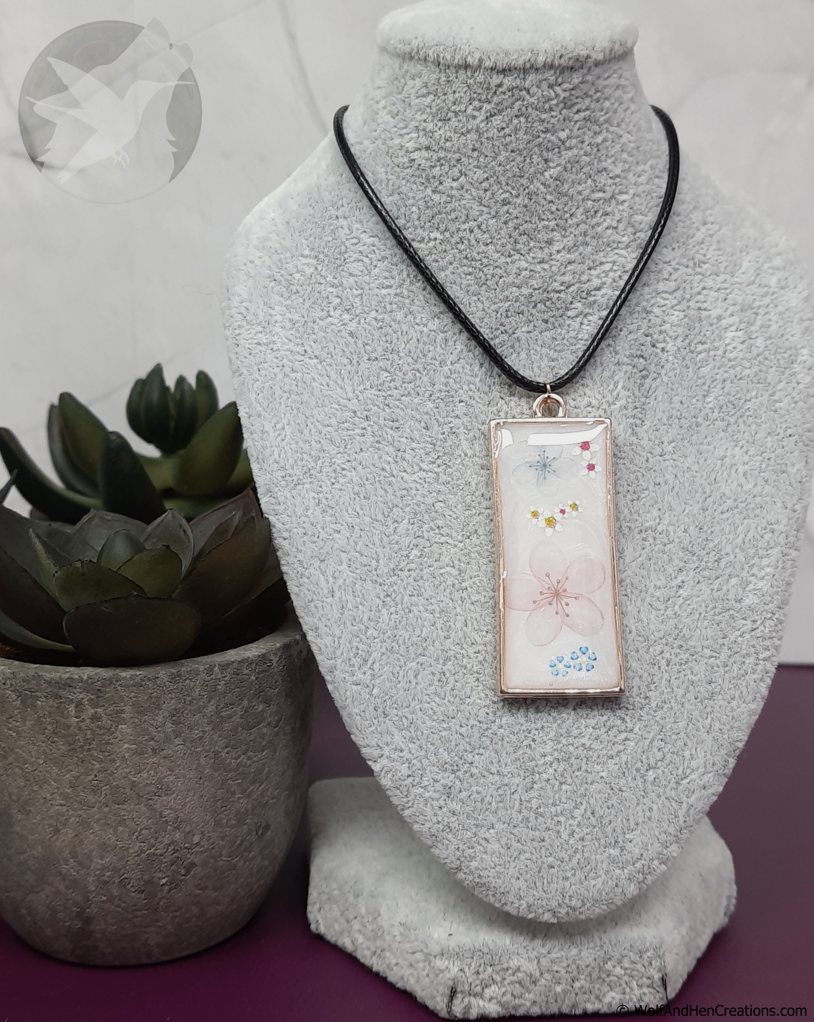 Necklace with a floral patterned pendant on a mannequin bust next to a potted plant