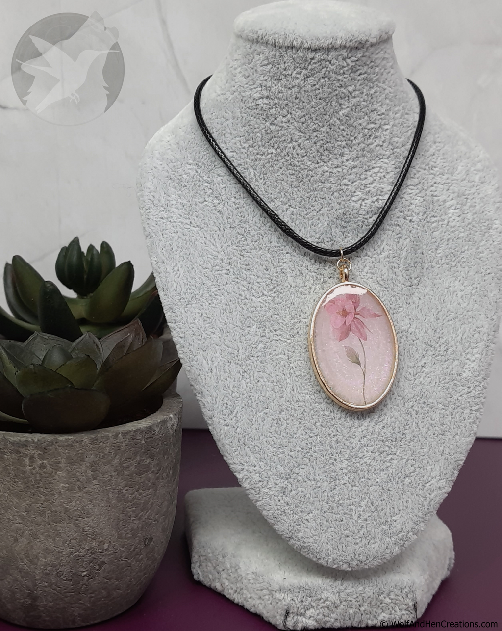 Necklace with a floral pendant on a mannequin bust next to a potted plant.