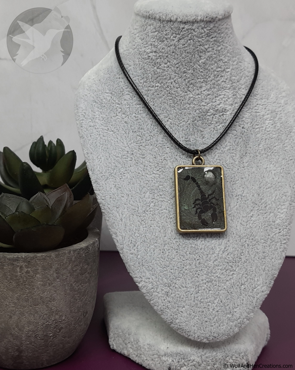 Necklace with a pendant on a textured gray stand with a plant in the background
