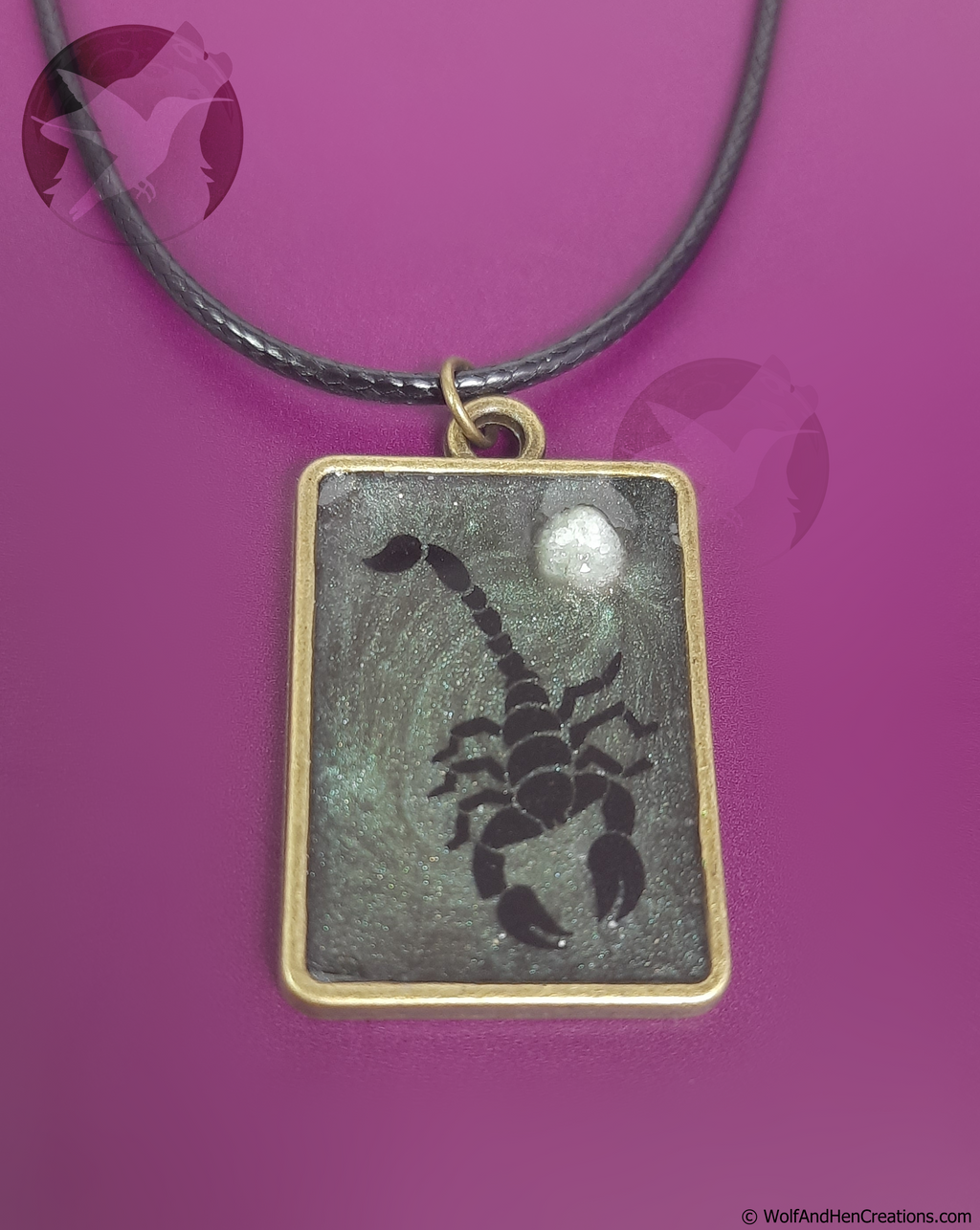 Scorpion pendant on a black cord against a purple background