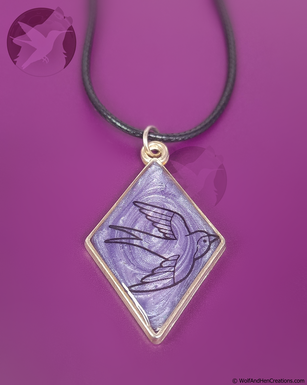 A diamond-shaped pendant necklace featuring a lilac background with a black bird illustration, set in a gold-tone frame and suspended from a black cord, shown against a solid purple background.