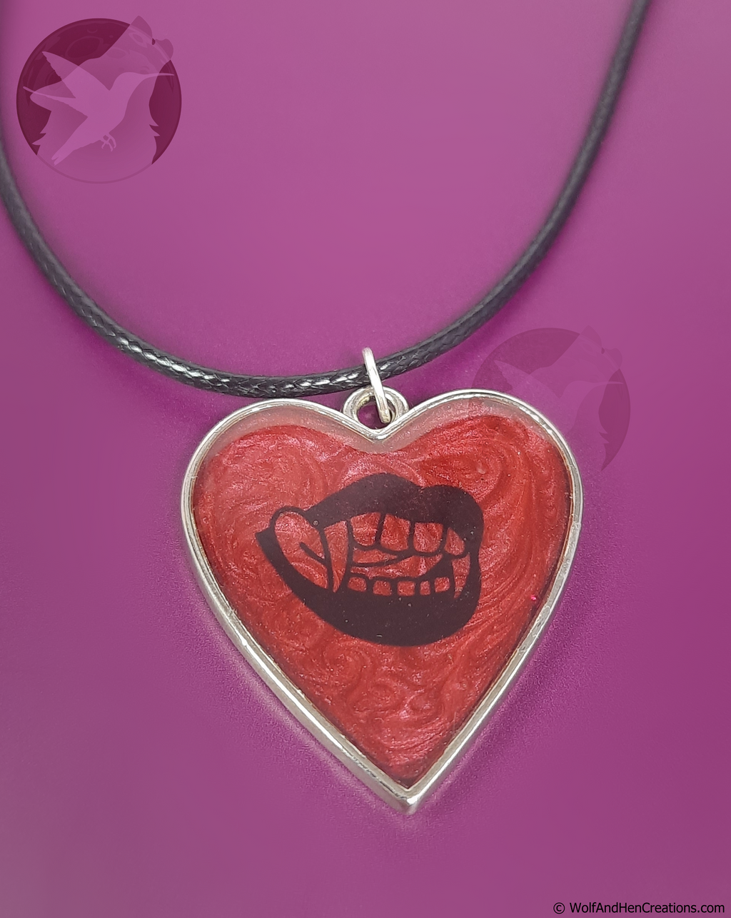 A heart-shaped pendant necklace featuring a red marbled background with a black graphic of lips with vampire teeth, suspended from a black cord on a purple background.