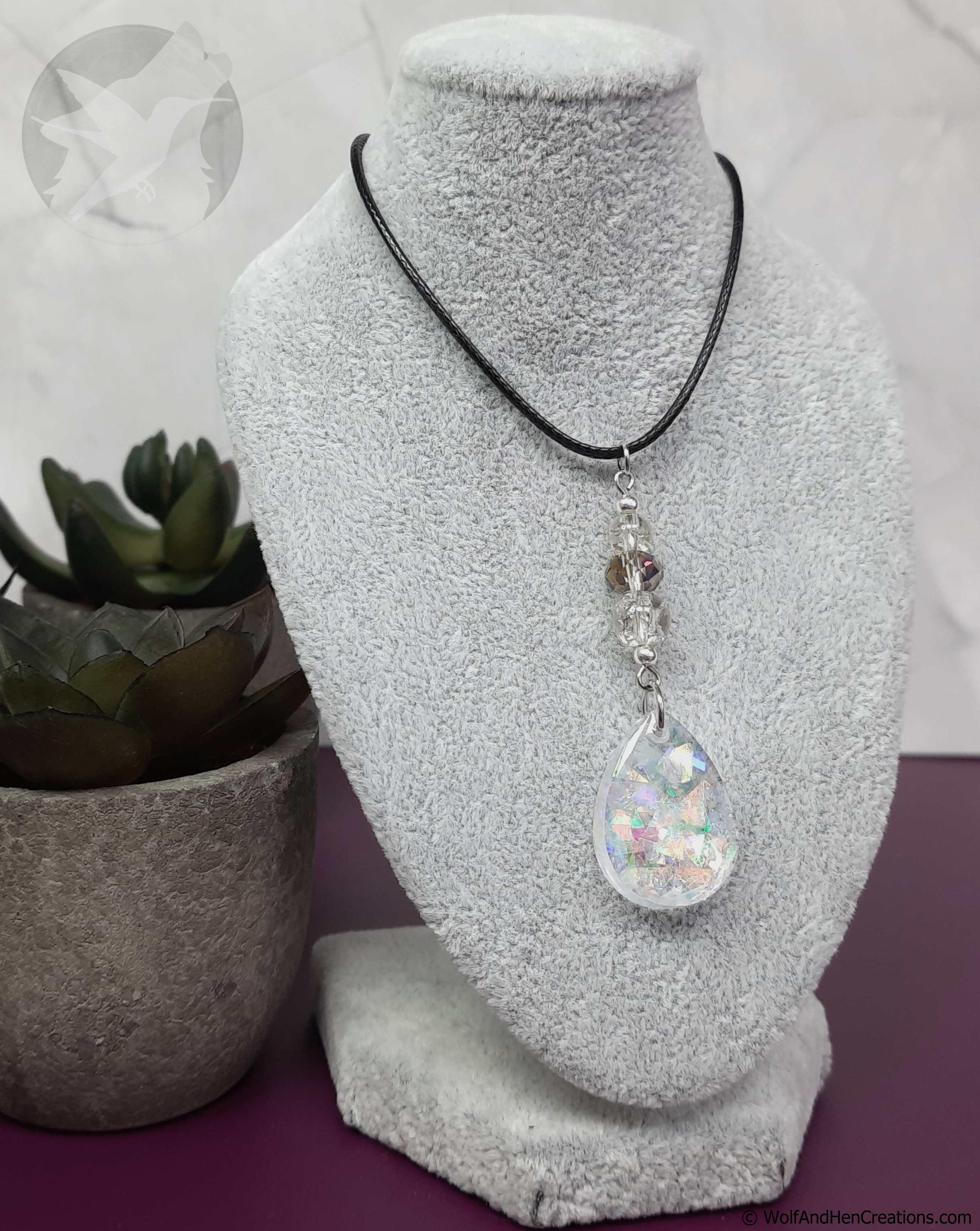 Necklace with a teardrop-shaped pendant on a gray bust with a plant in the background