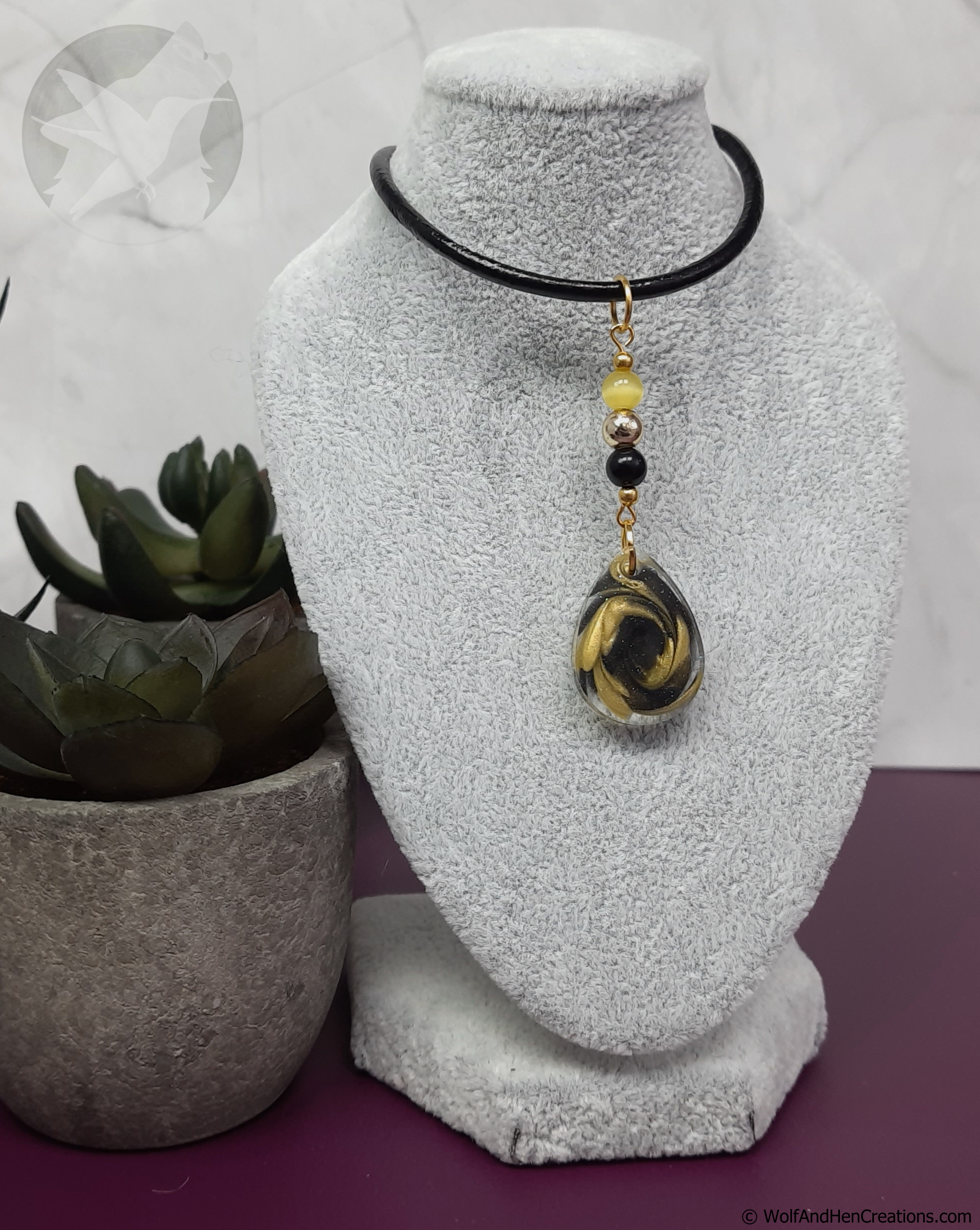 Necklace with a pendant on a white bust, next to a potted plant.