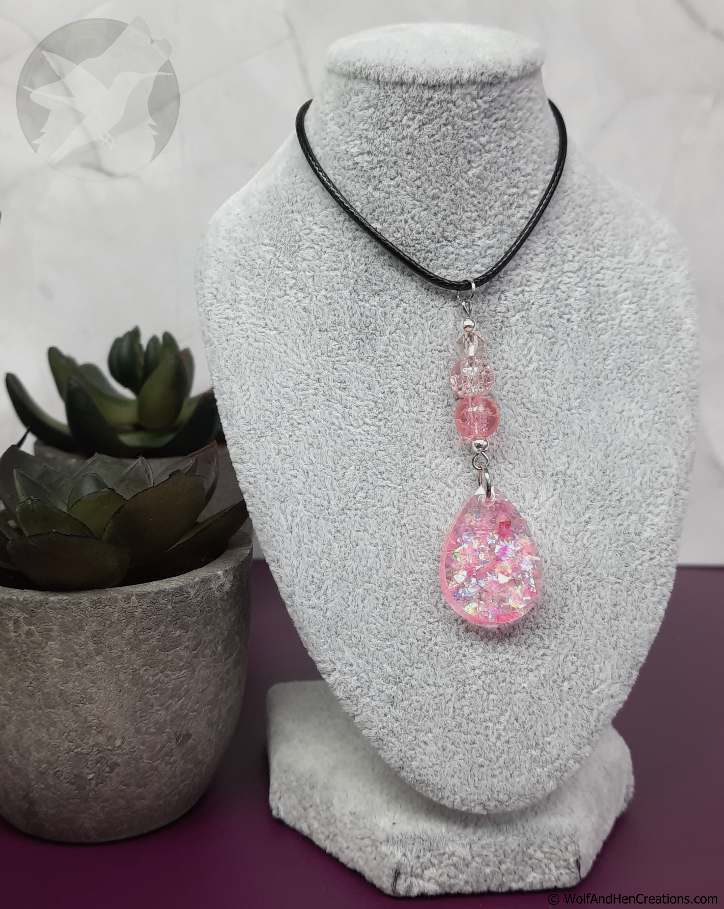 Necklace with a pink teardrop pendant on a textured stand with a plant in the background